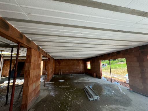 Intérieur d'un bâtiment en construction avec des murs en briques et des poutres au plafond.