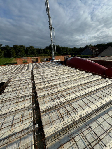 Vue d'un toit en construction avec des planches de béton et une grue en arrière-plan.