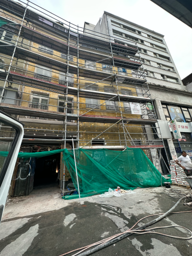 Façade d'immeuble en rénovation avec échafaudages et bâches vertes.