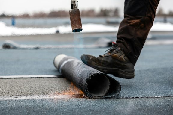 Personne debout sur un rouleau de matériau de construction, utilisant un chalumeau.
